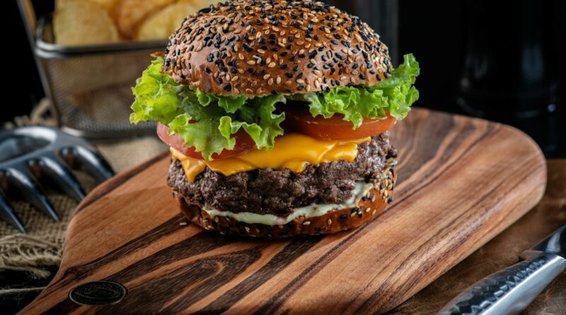 Close-up of a delicious cheeseburger with sesame seed bun and toppings on a wooden board.