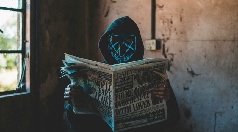 A person in a neon mask and hoodie reads a newspaper in an eerie, abandoned room.