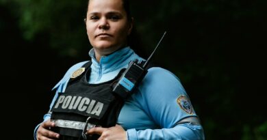 Female police officer in uniform standing outdoors with a confident expression and radio handset.