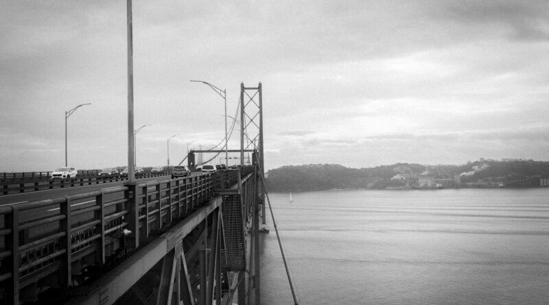 A black and white view of Ponte 25 de Abril bridge in Lisbon, Portugal, overlooking the river.