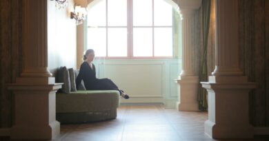 A woman in a black dress sits elegantly in a classic lobby framed by architectural columns.