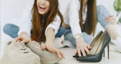 Crop exited young female in jeans and white shirts choosing between elegant glamour black high heels and comfortable trendy suede sneakers while sitting on floor together