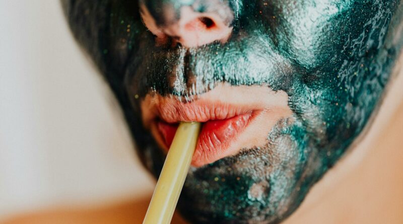 Close-up of woman with metallic facial mask sipping through a straw, embodying relaxation and modern skincare.