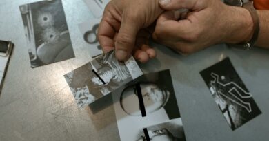 Close-up of handcuffed person examining crime scene photos on table, indicating investigation process.