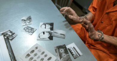 A prisoner in an orange jumpsuit reviews crime scene photos in a jail interrogation room.