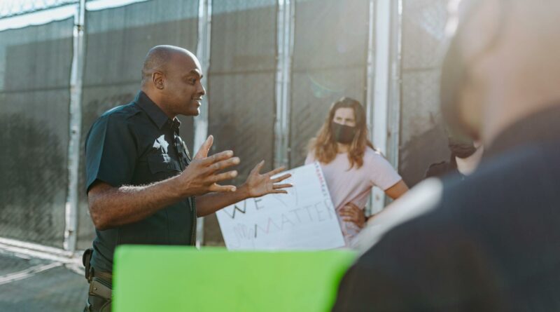 A police officer converses with protesters holding signs outdoors, demonstrating active communication.