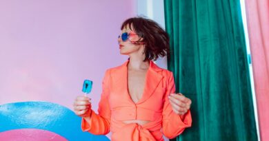 Trendy portrait featuring a woman in vibrant attire with sunglasses holding a blue lollipop.
