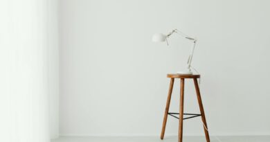 Simple minimalist setup with a white desk lamp placed on a wooden stool against a white wall.