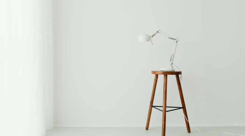 Simple minimalist setup with a white desk lamp placed on a wooden stool against a white wall.