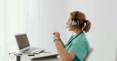 A female doctor using a laptop for an online consultation, wearing a headset in a bright office.