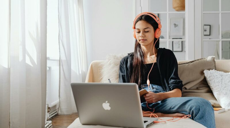 Teenage girl wearing headphones using a laptop for online learning at home in a cozy setting.