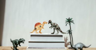 Vibrant dinosaur toys arranged on stacks of books against a plain background, creating a playful scene.