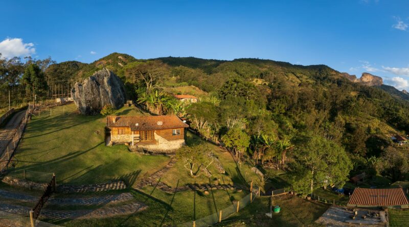 A serene aerial view of São Bento do Sapucaí's countryside, featuring a quaint house against a lush mountain backdrop.