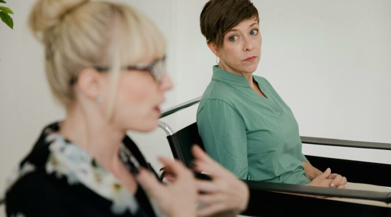 Two women engaged in a focused conversation indoors with contrasting attire.