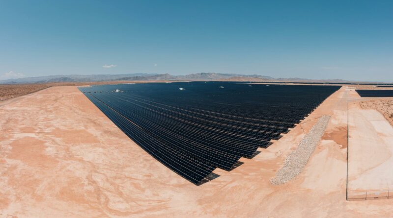 Aerial view of a large solar farm in a desert setting under a clear blue sky.