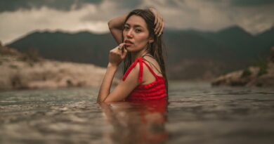 Young woman in red dress posing in a lake with scenic mountain backdrop in Potrerillos, Mendoza.