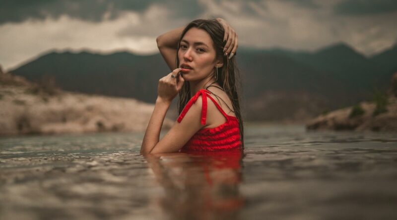 Young woman in red dress posing in a lake with scenic mountain backdrop in Potrerillos, Mendoza.