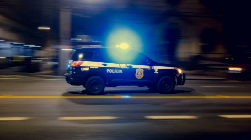 Blurred motion capture of a police car speeding at night with flashing lights on a city street.