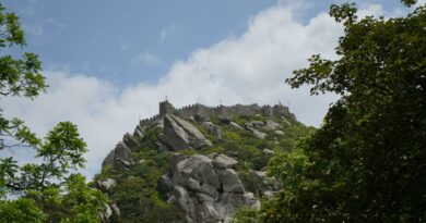 A captivating view of Castelo dos Mouros perched on a hill in Sintra, surrounded by lush greenery under a cloudy sky.