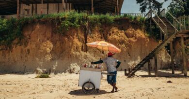 A beach vendor with an ice cream cart under an umbrella at Nazaré Beach, Brazil.