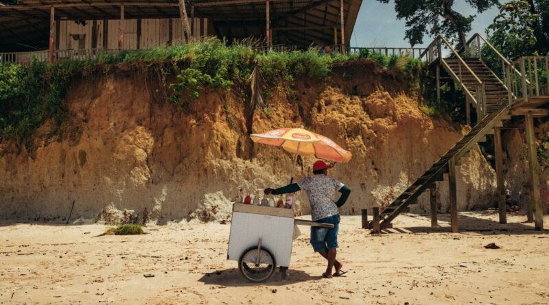 A beach vendor with an ice cream cart under an umbrella at Nazaré Beach, Brazil.