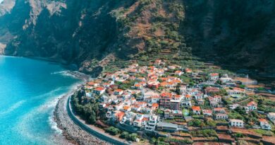 Stunning aerial view of a coastal town in Madeira, Portugal, with lush cliffs and turquoise sea.