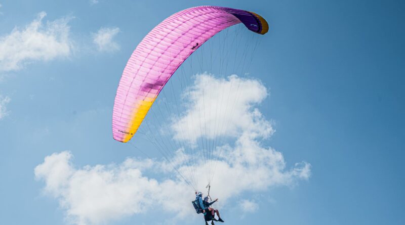 Experience the thrill of tandem paragliding with colorful parachute soaring high in the clear blue sky.