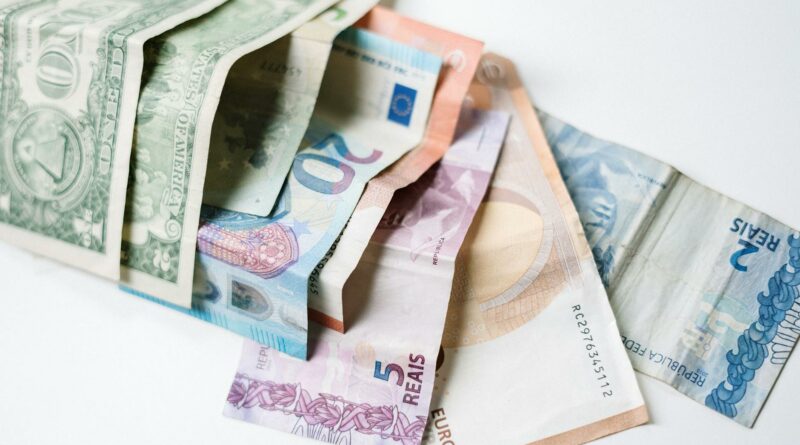 A collection of different international currency notes, including US Dollar, Euro, and Brazilian Real, on a white background.