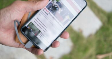 A hand holds a smartphone displaying online news while charging with a portable power bank.