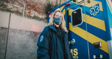 Female paramedic in a mask standing confidently by an EMS ambulance.