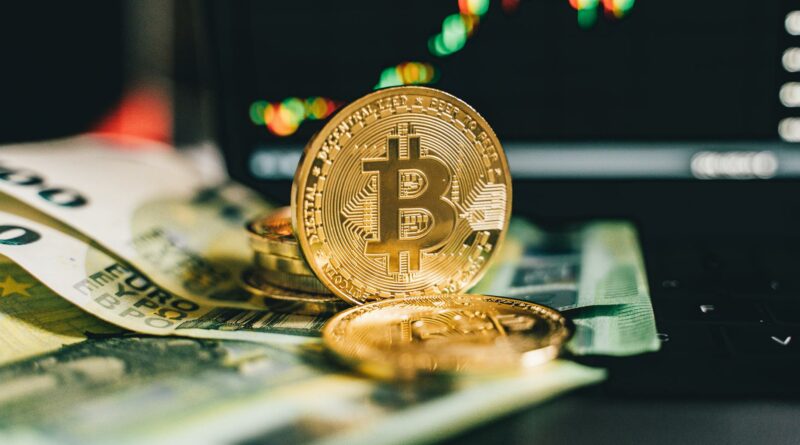 Close-up of Bitcoin and Euro notes on laptop keyboard with market chart in background.