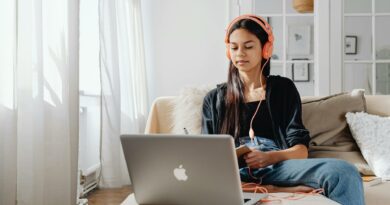 Teenage girl wearing headphones using a laptop for online learning at home in a cozy setting.