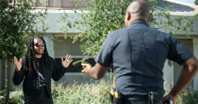 A police officer engages with a civilian raising hands outdoors, signifying communication or questioning.
