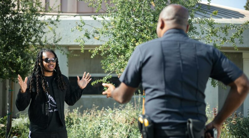 A police officer engages with a civilian raising hands outdoors, signifying communication or questioning.