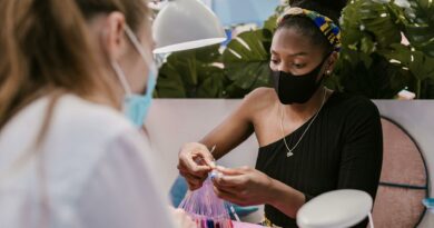 A nail technician and customer wearing masks in a modern salon choosing nail polish colors, embracing safety measures.