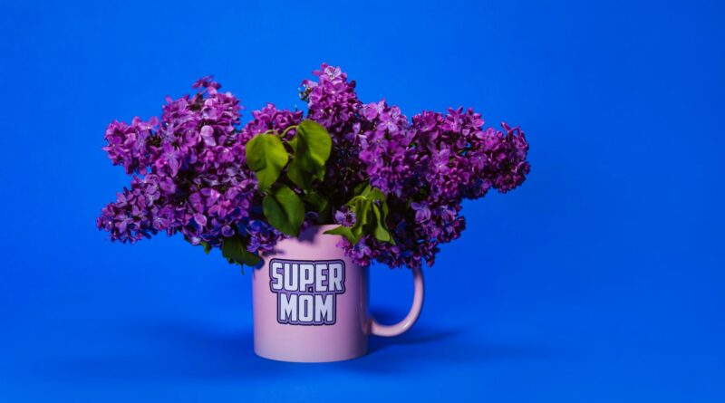 Purple lilacs in a pink Super Mom mug against a bold blue backdrop.