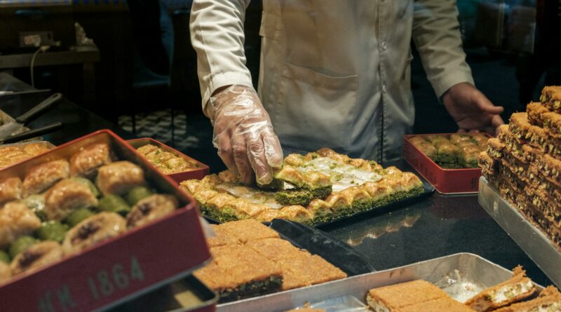 From above of anonymous crop male in gloves and white robe putting delicious fresh sweet dessert in container in local bakery shop