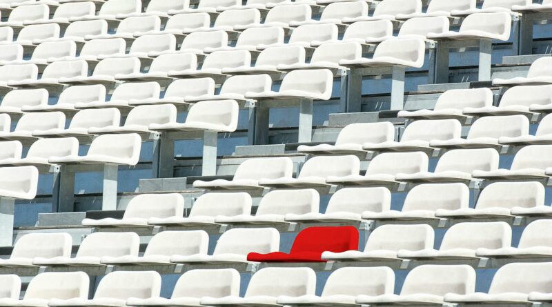 A striking red chair stands out in a sea of white stadium seats, symbolizing individuality.