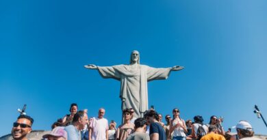 Tourists gather at the iconic Christ the Redeemer statue under clear blue skies in Rio de Janeiro, Brazil.