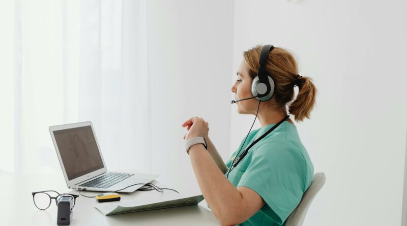 A female doctor using a laptop for an online consultation, wearing a headset in a bright office.