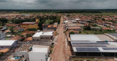 Vista aérea de torres de transmissão de energia em paisagem brasileira com turbinas eólicas ao fundo, simbolizando a integração de renováveis na rede elétrica.