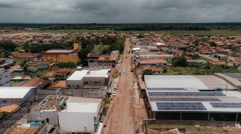 Vista aérea de torres de transmissão de energia em paisagem brasileira com turbinas eólicas ao fundo, simbolizando a integração de renováveis na rede elétrica.