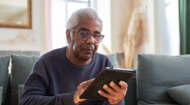 Idoso utilizando um tablet com auxílio, simbolizando a inclusão digital e o aprendizado de novas tecnologias.