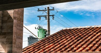 Painéis solares em telhados de casas e edifícios, com linhas de transmissão de energia e uma cidade ao fundo, simbolizando a integração da geração distribuída e as redes elétricas modernas no Brasil.