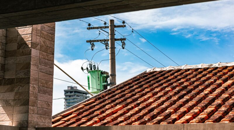 Painéis solares em telhados de casas e edifícios, com linhas de transmissão de energia e uma cidade ao fundo, simbolizando a integração da geração distribuída e as redes elétricas modernas no Brasil.
