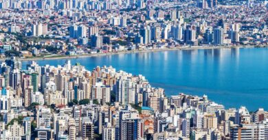 Reservatório de água com nível baixo em uma região árida do Brasil, com casas ao fundo, simbolizando a crise hídrica.