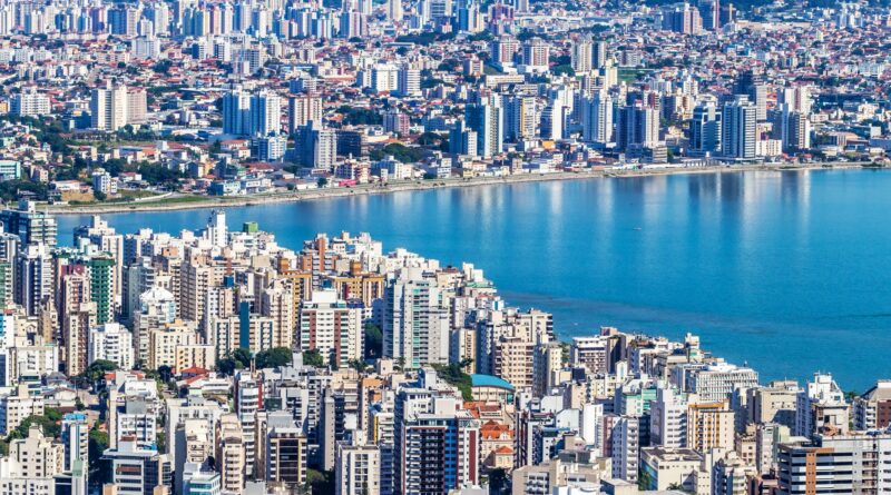 Reservatório de água com nível baixo em uma região árida do Brasil, com casas ao fundo, simbolizando a crise hídrica.