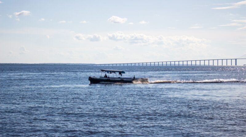 Balsas carregadas navegando em um rio largo no Brasil, com margens verdes e céu azul, simbolizando o transporte hidroviário e o potencial logístico do país.