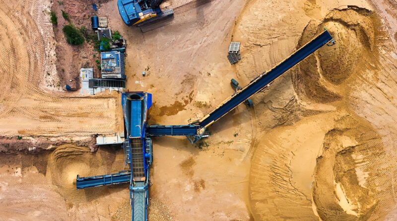 Mão segurando minerais brutos com fundo de turbinas eólicas e painéis solares, simbolizando a transição energética