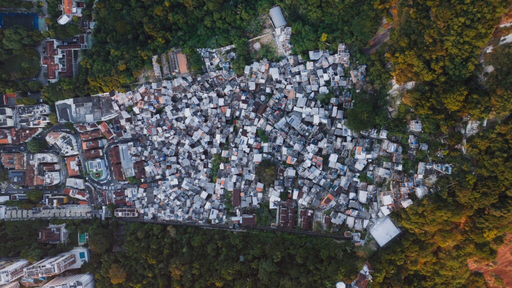 Vista aérea de uma área urbana com casas em diferentes estágios de formalização, com sobreposição de um mapa ou planta baixa, simbolizando a regularização fundiária no Brasil.